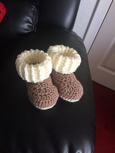 a pair of crocheted baby booties sitting on top of a black leather chair