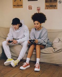 two people sitting on a couch holding remotes and looking at the same person's camera