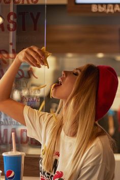 a woman in a red hat eating food at a fast food restaurant while holding a drink