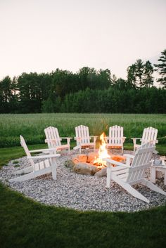 a fire pit with chairs around it in the middle of some grass and gravel area