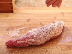 a raw piece of meat on a cutting board with seasoning sprinkles