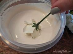 a person is holding a flower in a plastic container with white paint on it and there are flowers around the bowl