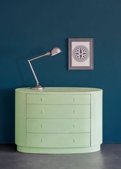 a green chest of drawers with a lamp on top in front of a blue wall