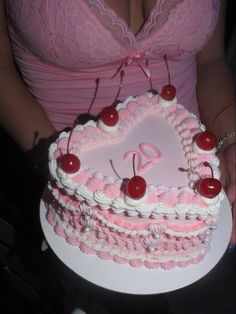 a woman holding a heart shaped cake with cherries on the top and pink icing