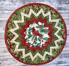 a red bird sitting on top of a green and white christmas wreath table mat with holly leaves