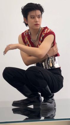 a man sitting on top of a glass table wearing black pants and a red shirt