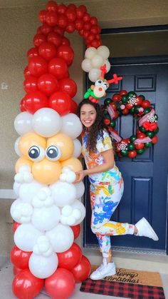 a woman standing next to a bunch of balloons in the shape of santa's face