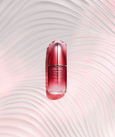 a bottle of red liquid sitting on top of a white and pink wave patterned surface