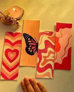 a hand is holding four cards with different designs on them and a candle in the background