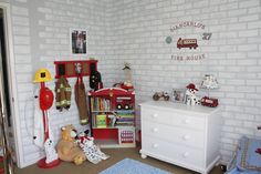 there is a fire truck themed bedroom with toys on the dresser and bookshelf