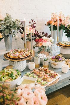 a table topped with lots of food next to tall vases filled with pink flowers