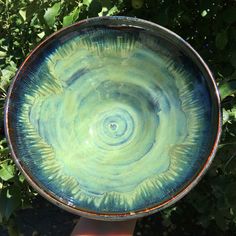 a blue and green bowl sitting on top of a wooden table next to some bushes