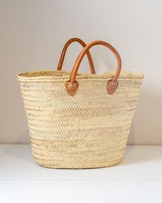 a large woven basket with leather handles on a white countertop next to a wall