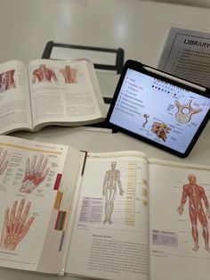 an open book with diagrams on it and a tablet showing the human body's muscles