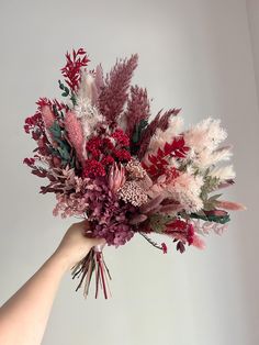 a hand holding a bouquet of flowers on a white background with red and pink foliage