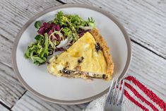 a white plate topped with a slice of quiche next to a salad and fork