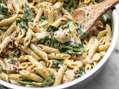 a white bowl filled with pasta and spinach covered in sauce, topped with a wooden spoon