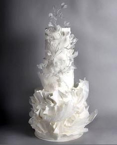 a three tiered white wedding cake with flowers on the top and bottom, in front of a gray background