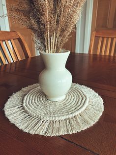 a white vase sitting on top of a wooden table next to a rug covered in grass