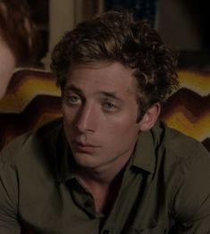 a man with curly hair sitting in front of a mirror