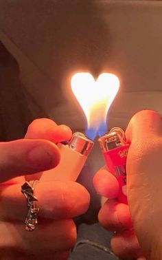 someone holding two lighters in their hands with a heart shaped light on top of them