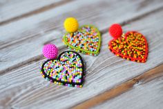 three heart shaped beaded brooches sitting on top of a wooden table next to each other