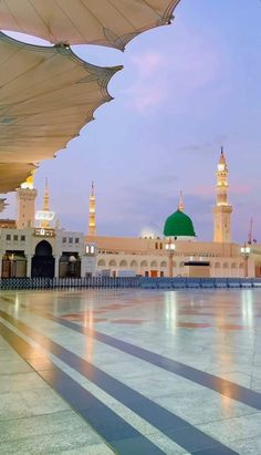 an empty courtyard in front of a large white building with green dome and lights on it