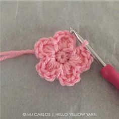 the crochet flower is being worked on by a pink yarn hook and thread