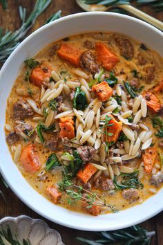 a white bowl filled with pasta, meat and vegetables on top of a wooden table