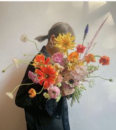 a woman holding a bouquet of flowers in front of her face and looking at the wall