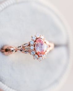 a pink diamond ring sitting on top of a white cushion