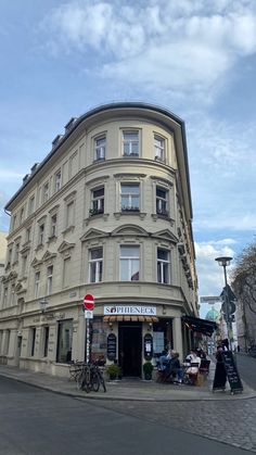 an old building on the corner of a street with people sitting at tables in front of it