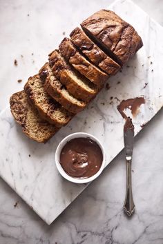 sliced loaf of bread on a marble board with chocolate sauce in a small bowl next to it