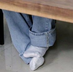 a person's feet with white socks underneath a wooden table and legs wearing blue jeans