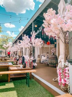 an outdoor area with tables, benches and pink flowers on the trees in front of it