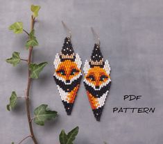 a pair of beaded earrings with an orange and black bird on the front, sitting next to a plant