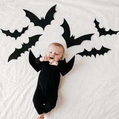 a baby is laying on the bed with bats cut out of it's back