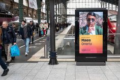 people walking on the sidewalk in front of a train station with an advertisement for mass cinema