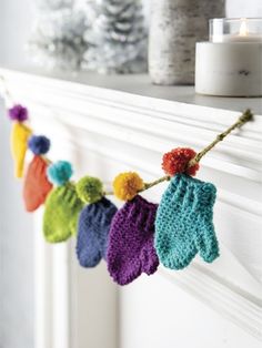 colorful knitted mittens hanging from a mantel with candles in the background on a mantle