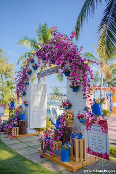 the entrance to an event decorated with purple flowers and potted plants is shown in front of a palm tree