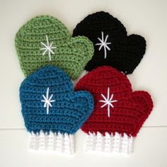 four crocheted mittens are lined up on a white surface, one is black, one is green and the other is red