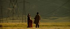 two people standing in an open field with power lines in the back ground and hills in the background