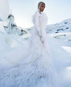 a woman in a white gown standing in the snow with her hands on her hips