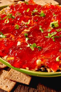 a green bowl filled with pizza sauce and crackers on top of a wooden table