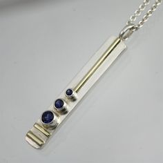 Sterling silver and 14 karat gold necklace with lab-grown Sapphire stones. Very contemporary and classy. Comes on an 18" sterling chain with the artist's tag attached at the clasp. Fabricated by hand using 6x2mm rectangle sterling wire cut with a jeweler's saw, stamped with the artist's initials and polished. Pieces of sterling tubing are cut and soldered to the front along with 14 karat gold wire and a sterling bail. The fine silver is raised to the surface to remove firescale and prevent tarni Tube Setting, Contemporary Jewellery Necklace, Precious Metal Clay Jewelry, Diy Jewelry Pendants, Silver Pendent, Modern Silver Jewelry, Bezel Jewelry, Sapphire Stones