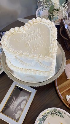 a heart shaped cake sitting on top of a wooden table next to plates and flowers