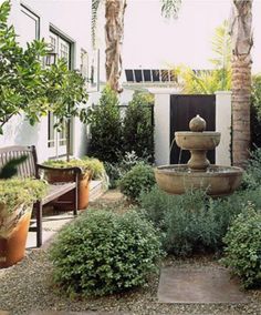 a fountain in the middle of a garden surrounded by potted plants and other greenery