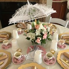 the table is set with pink and white plates, cups, and an umbrella on it