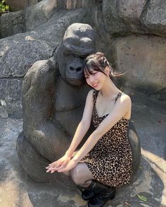 a woman sitting on top of a rock next to a statue of a gorilla bear