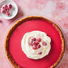 a pie with white frosting and cranberries on top sitting on a pink surface